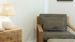 Ein Zimmer mit einem Holzsessel, einem Nachttisch mit Lampe und einem gerahmten Bild an der Wand.