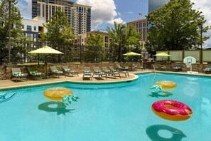 Ein Swimmingpool mit Liegestühlen und Sonnenschirmen, umgeben von Bäumen und Gebäuden.