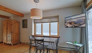 Ein Essbereich mit Tisch und Stühlen, einem Holzschrank, einem an der Wand befestigten Fernseher und einem Fenster mit Aussicht.