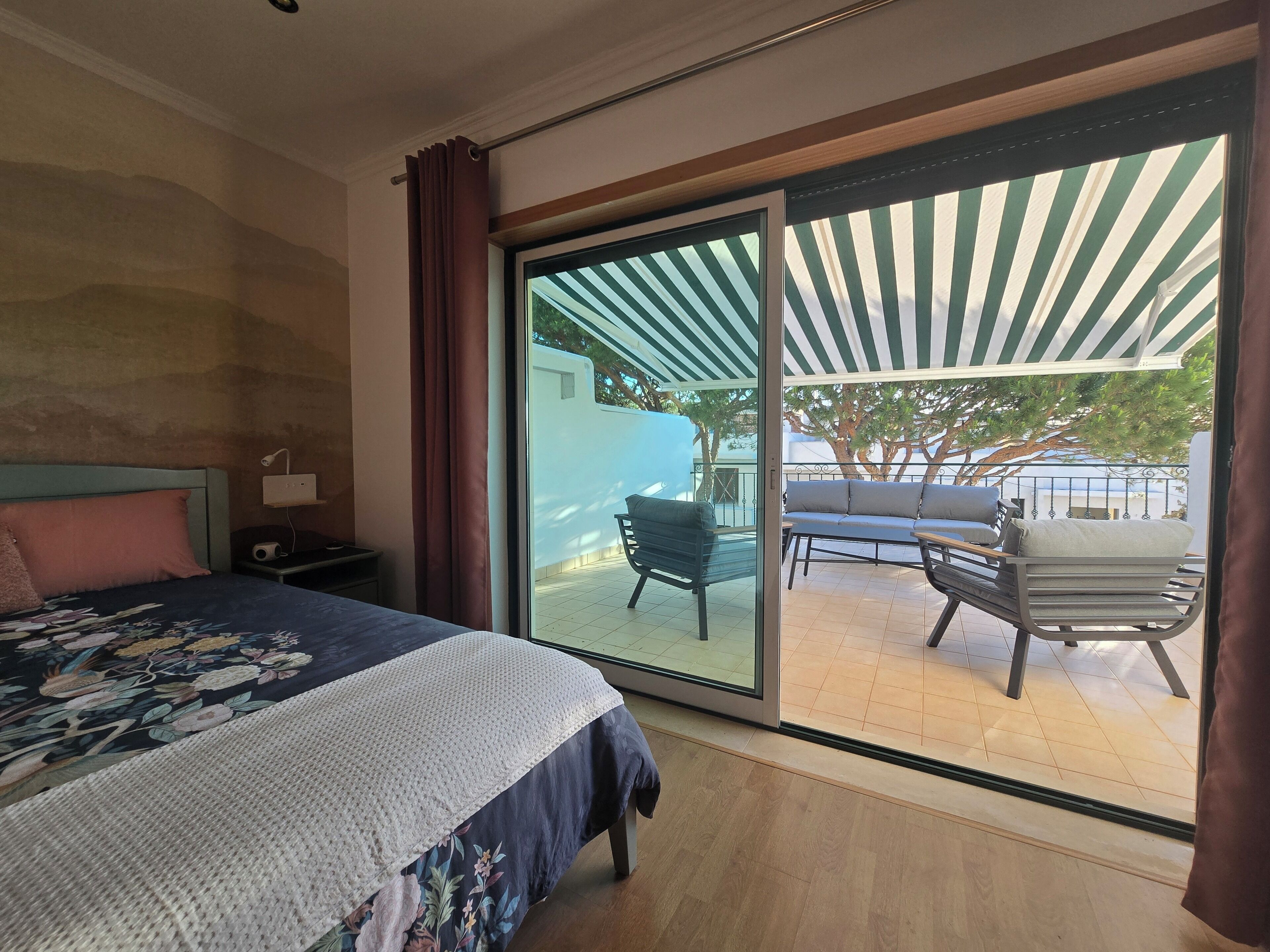 A bedroom with a bed, a nightstand, a large sliding glass door leading to an outdoor seating area with a table and chairs.