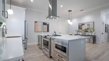 Une cuisine moderne dotée d’appareils électroménagers en acier inoxydable, d’un îlot central et de luminaires suspendus.