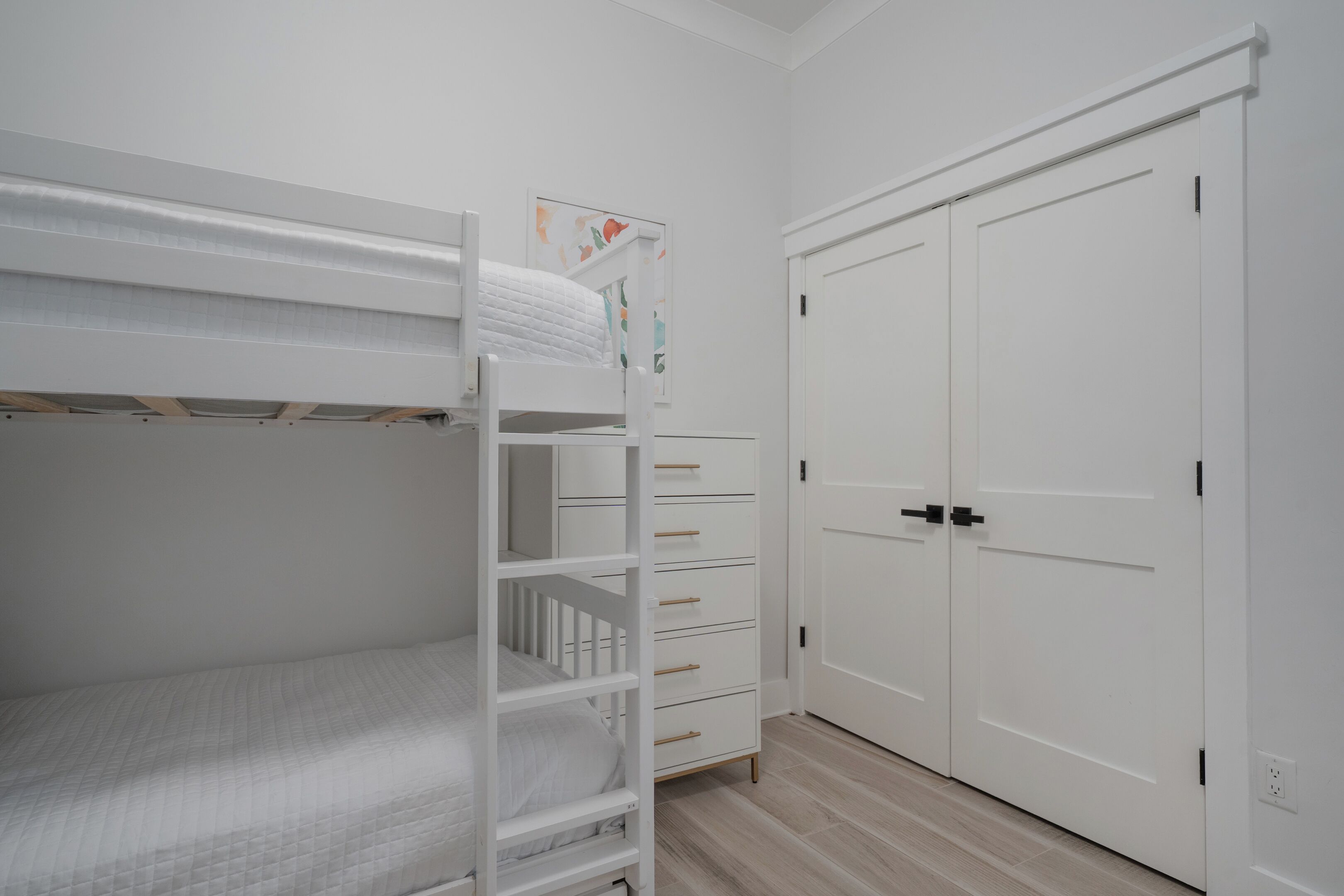 A room with a bunk bed, a dresser with drawers, and a set of double doors.