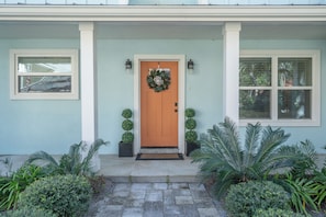 Une maison avec une porte d’entrée, une guirlande, deux plantes en pot et une fenêtre.