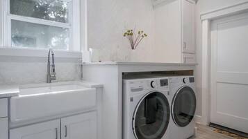 A laundry room with a washing machine, a sink, and a window.