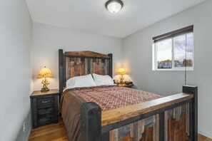 A bedroom with a wooden bed, two bedside tables with lamps, a window with a view, and a ceiling light.