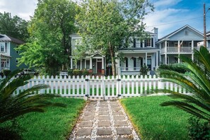 Une rue résidentielle bordée d’une clôture en bois peinte en blanc, d’un chemin de pierre et de maisons dotées de vérandas.