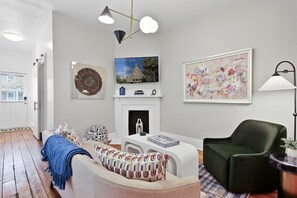 A living room with a fireplace, a sofa, a green armchair, and artwork on the walls. - Savannah Home * Firepit * Dogs OK * Free Parking (Savannah)