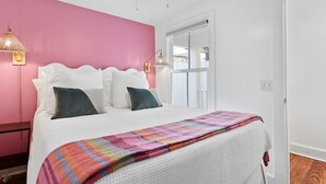 Una camera da letto con un letto, una parete rosa, una finestra e una lampada.