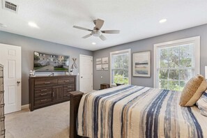 Une chambre à coucher avec un lit, un ventilateur de plafond, une commode et une fenêtre avec des stores.