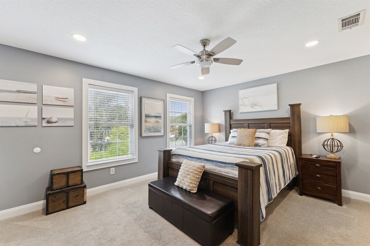 A bedroom with a bed, a ceiling fan, a window, a nightstand, and a bench.