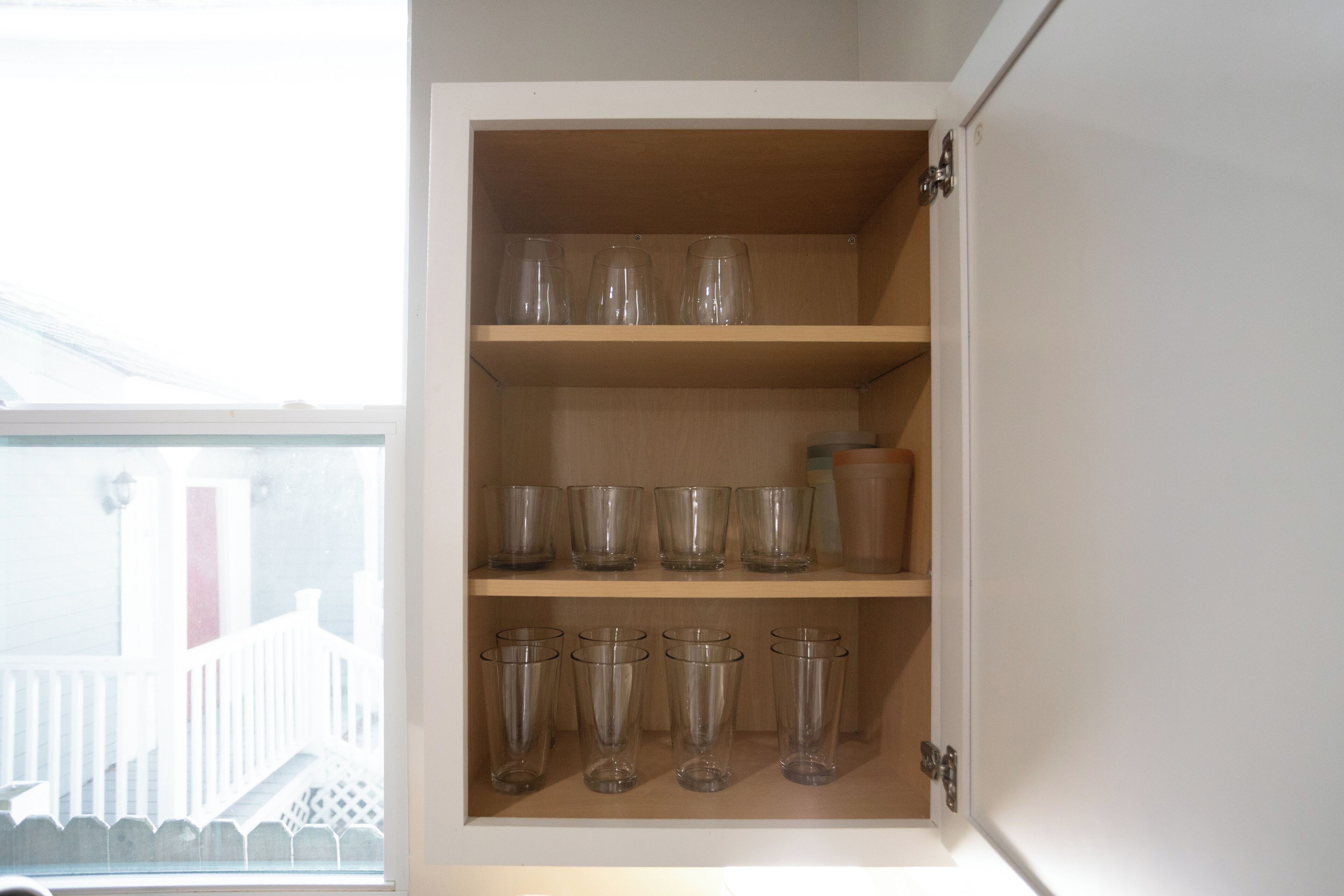 Un mueble de cocina con varios estantes, cada uno con vasos de vidrio transparente y un recipiente marrón.