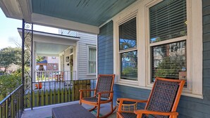 Eine Veranda mit zwei Schaukelstühlen und einem kleinen Tisch, ein Holzzaun und ein Haus im Hintergrund.