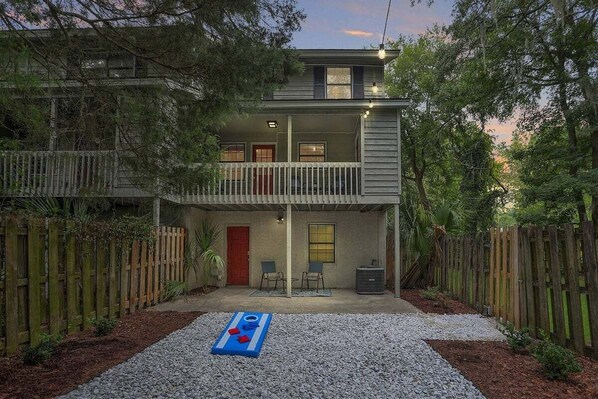 A two-story house with a balcony, a patio with chairs, and a shuffleboard table.