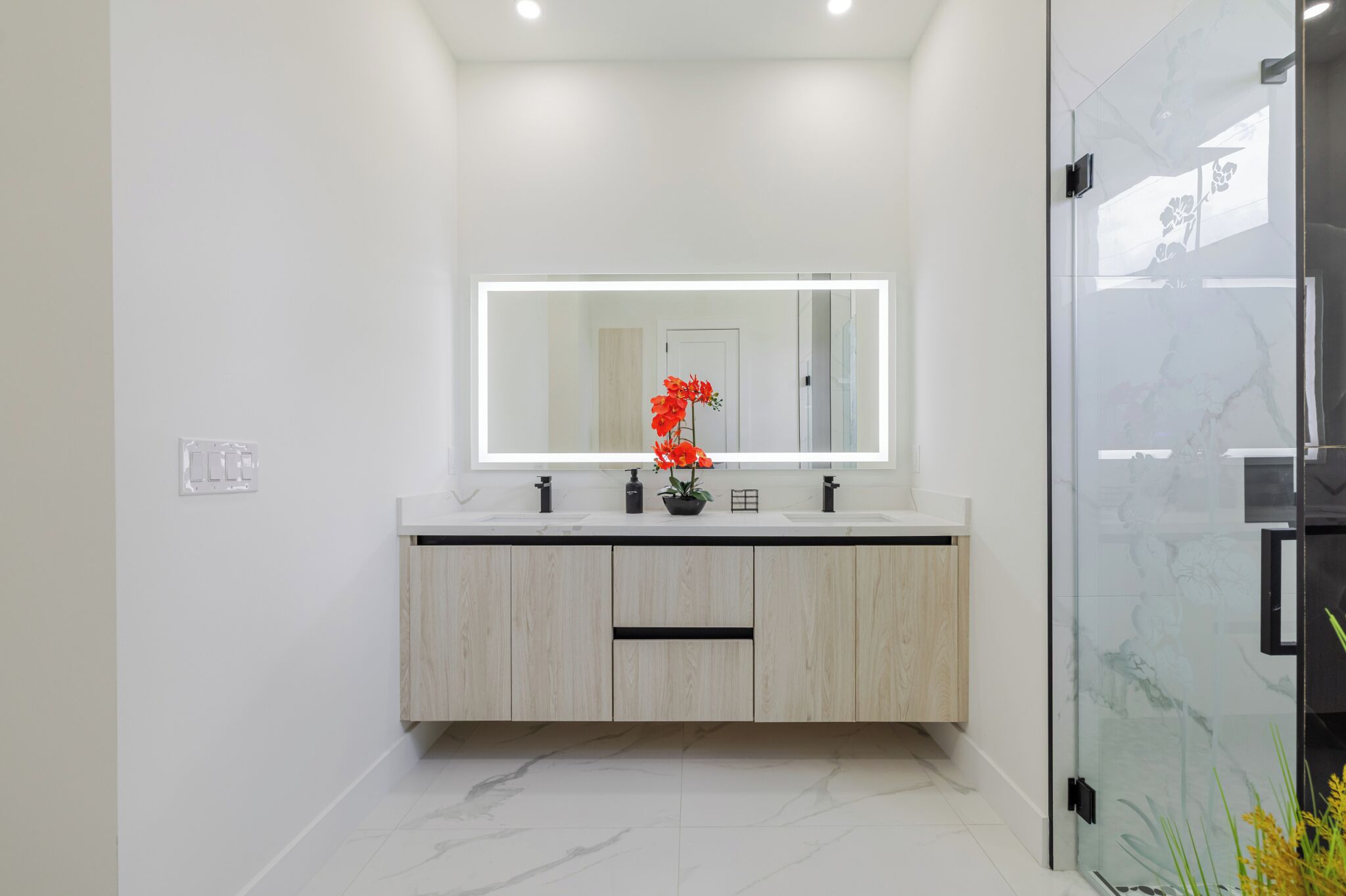 Un baño moderno con un espejo grande, dos lavamanos y una cabina de ducha de vidrio.