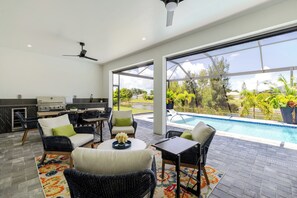 A modern outdoor kitchen with a dining area, a ceiling fan, and a view of a swimming pool. - Chic Canal Front Retreat w/ Pool & Outdoor Kitchen (Cape Coral)