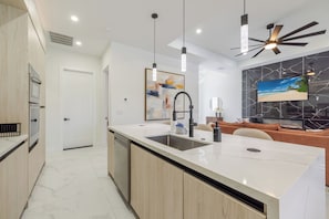 A modern kitchen with a large island, built-in oven, and pendant lighting. - Chic Canal Front Retreat w/ Pool & Outdoor Kitchen (Cape Coral)