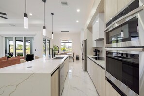A modern kitchen with a large island, stainless steel appliances, and pendant lighting. - Chic Canal Front Retreat w/ Pool & Outdoor Kitchen (Cape Coral)