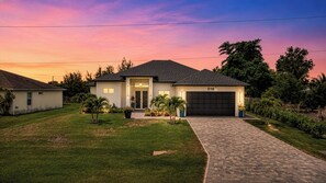 A single-story house with a garage, a driveway, and a well-maintained lawn. - Chic Canal Front Retreat w/ Pool & Outdoor Kitchen (Cape Coral)