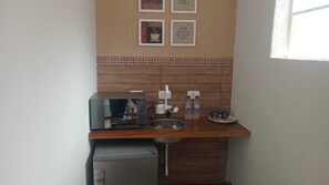 Una kitchenette compacta con cafetera, un lavamanos pequeño y un refrigerador.