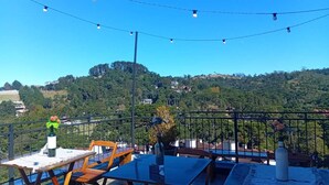 Una terraza con mesas y sillas, una barandilla y vistas a un paisaje montañoso.