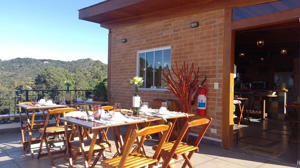 An outdoor dining area with tables and chairs, a fire extinguisher, and a view of the hills.