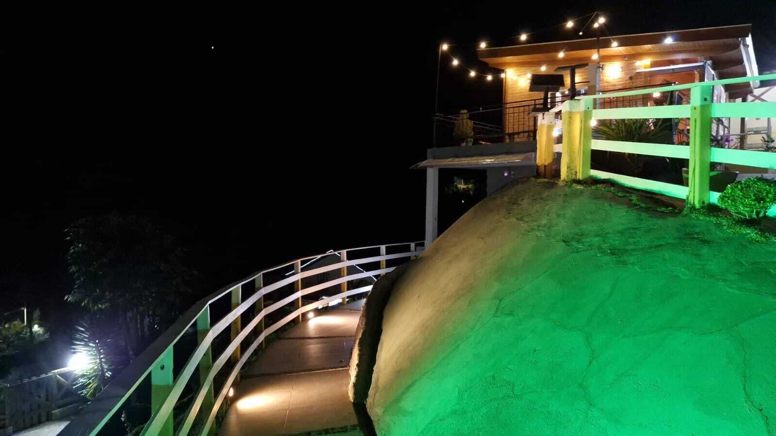 Vista noturna de um caminho sinuoso que leva a um edifício com luzes de corda e área coberta.