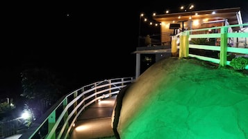 Vista noturna de um caminho sinuoso que leva a um edifício com luzes de corda e área coberta.