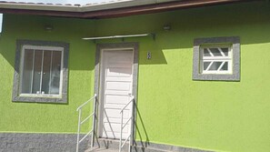 Un bâtiment à l’extérieur vert, avec une porte blanche et deux fenêtres aux cadres blancs.