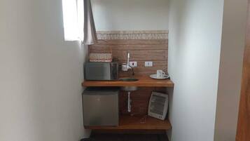 Eine kompakte Küchenzeile mit Mikrowelle, kleinem Kühlschrank, Spüle und Ventilator.