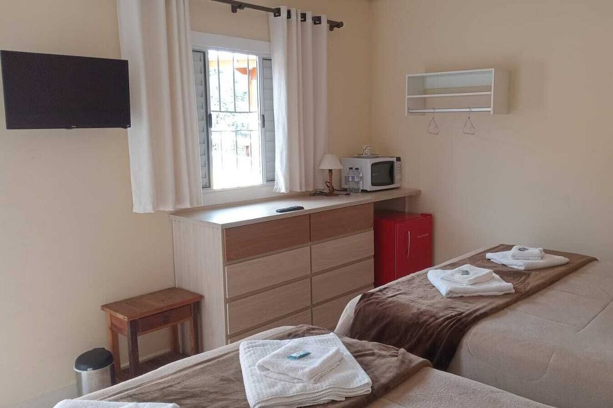 A hotel room with two beds, a small table, a microwave, a TV, and a window with curtains.