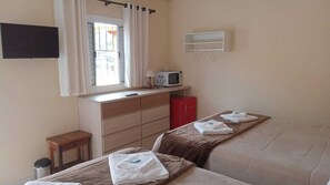 Habitación de hotel con dos camas, una mesita, microondas, televisor y ventana con cortinas.