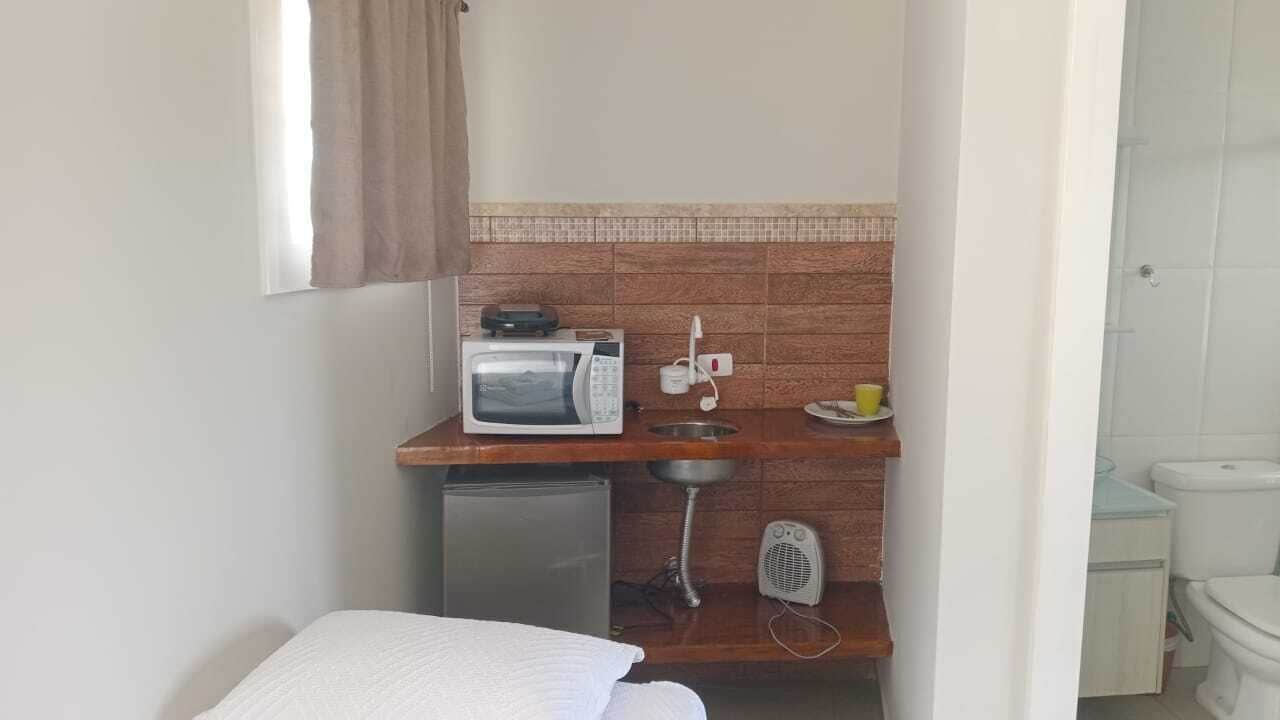 Una kitchenette compacta con microondas, pileta y heladera pequeña.