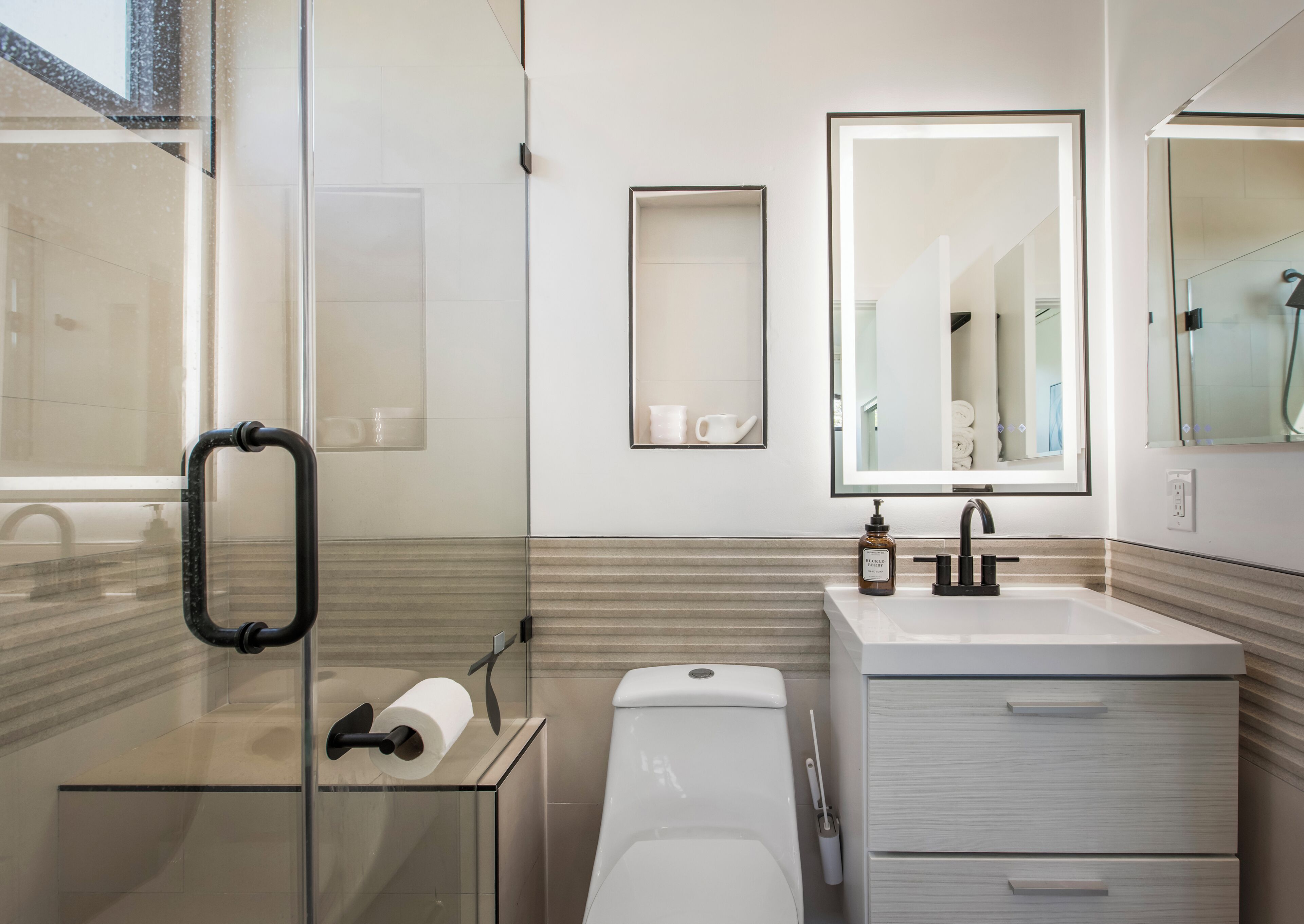 Un baño moderno con cabina de ducha de vidrio, inodoro blanco, lavabo con espejo y toallero.