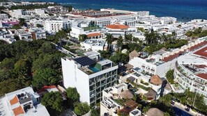An aerial view of a coastal city with a mix of modern and traditional architecture, including a prominent building with a green roof and solar panels. - Ocean-View King Studio with Private Balcony & Rooftop Pool (Playa del Carmen)