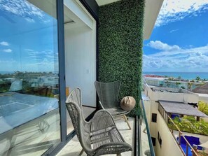 A balcony with wicker chairs, a glass table, and a view of the ocean and cityscape. - Ocean-View King Studio with Private Balcony & Rooftop Pool (Playa del Carmen)