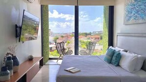 A bedroom with a bed, a TV, a chair, and a balcony with a view. - Ocean-View King Studio with Private Balcony & Rooftop Pool (Playa del Carmen)