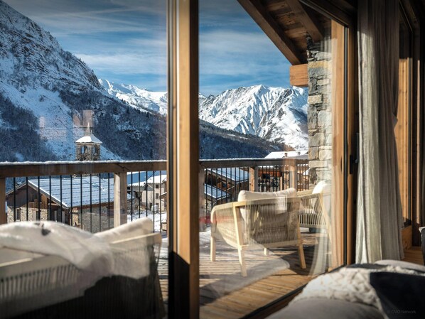 A room with a view of snow-covered mountains, a wooden balcony, and a stone wall.