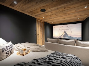 A modern room with a wooden ceiling, a large flat-screen TV, a sofa, and a bed with a blanket and pillows.