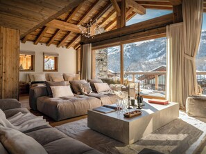 A cozy living room with a large sectional sofa, a coffee table, and a view of snowy mountains through large windows.