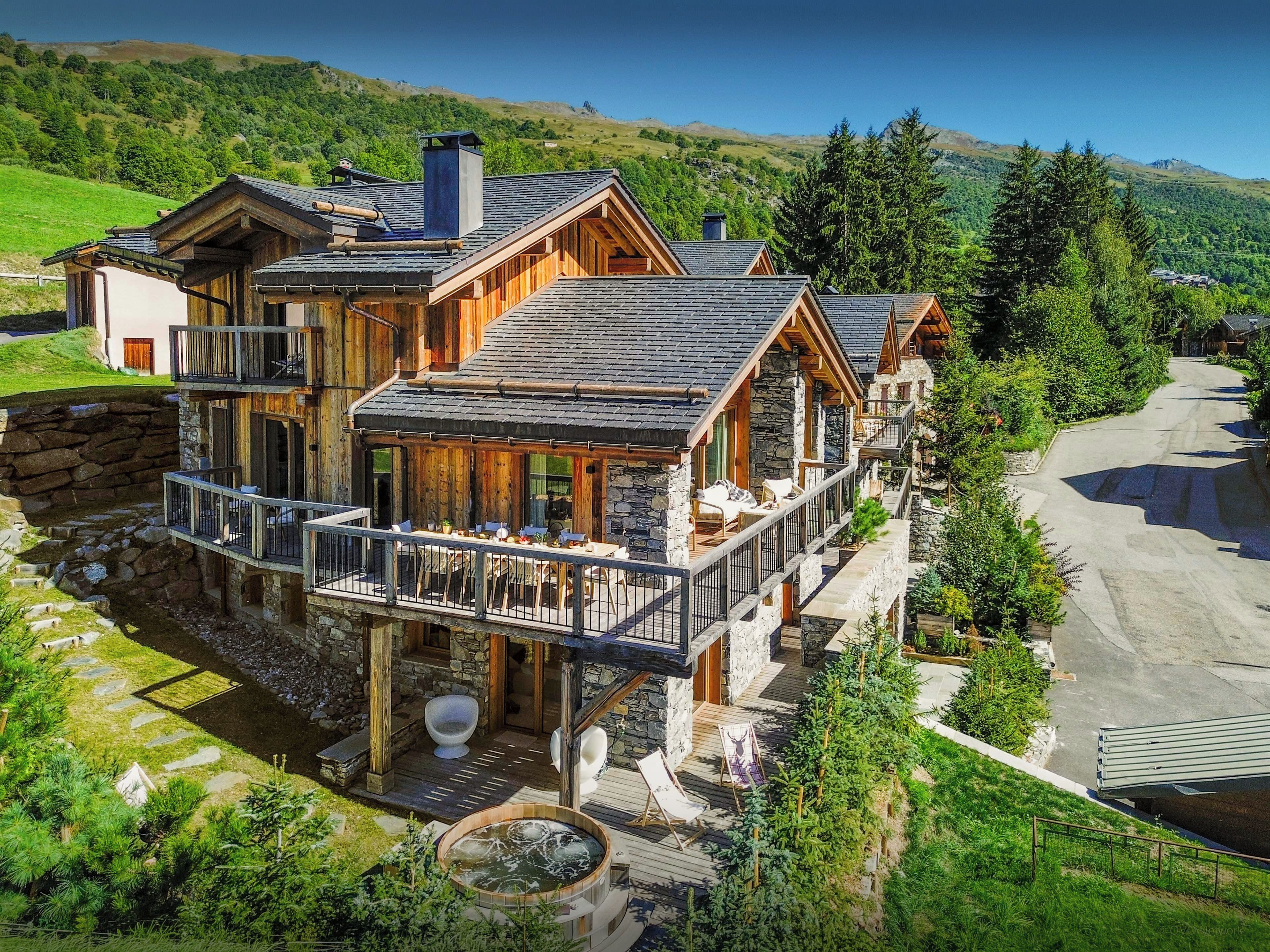 Una cabaña de madera de varios pisos con base de piedra, asientos exteriores y un jacuzzi.