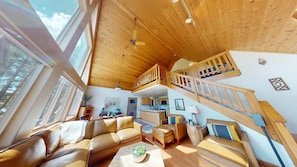 Ein geräumiger Wohnbereich mit hohen Decken, einer Holztreppe und großen Fenstern.