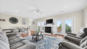 A spacious living room with a fireplace, comfortable seating, and a large clock on the wall.