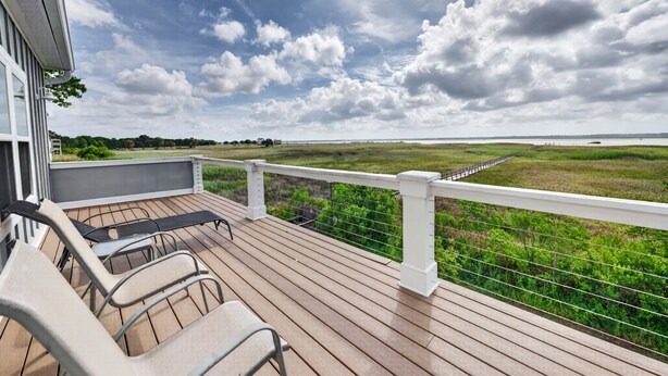 A wooden deck with outdoor seating and a view of a grassy field.