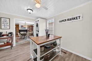 A kitchen with a wooden table, a wall-mounted sign reading 'SUPER MARKET,' and a ceiling fan. - Historic Kings on Queen Cottage in Georgetown's Historic District, just 10 min to beach. (Georgetown)