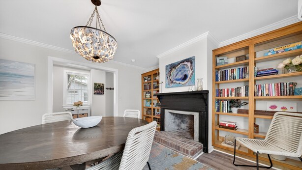 A dining area with a wooden table and chairs, a fireplace, and a bookshelf filled with books. - Historic Kings on Queen Cottage in Georgetown's Historic District, just 10 min to beach. (Georgetown)