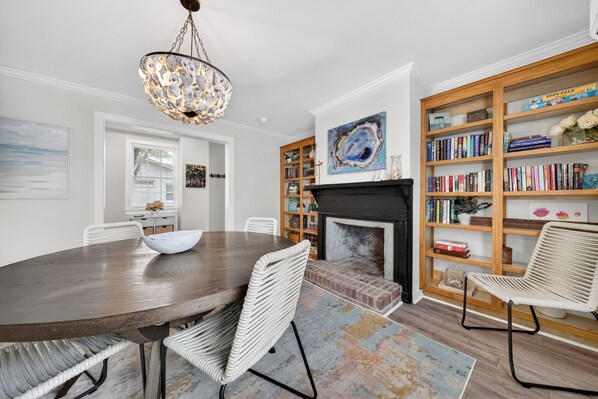 A dining area with a wooden table and chairs, a fireplace, and a bookshelf filled with books. - Historic Kings on Queen Cottage in Georgetown's Historic District, just 10 min to beach. (Georgetown)