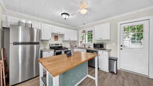 A kitchen with white cabinets, stainless steel appliances, a wooden island, and a ceiling fan. - Historic Kings on Queen Cottage in Georgetown's Historic District, just 10 min to beach. (Georgetown)