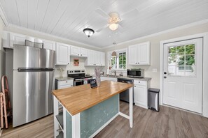 A kitchen with white cabinets, stainless steel appliances, a wooden island, and a ceiling fan. - Historic Kings on Queen Cottage in Georgetown's Historic District, just 10 min to beach. (Georgetown)