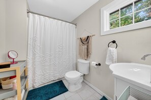 A bathroom with a toilet, sink, shower curtain, and a window with a view of trees. - Historic Kings on Queen Cottage in Georgetown's Historic District, just 10 min to beach. (Georgetown)