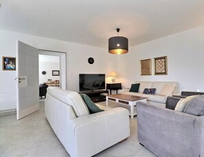 Un salon moderne comprenant un canapé, un fauteuil, un téléviseur, une lampe et des œuvres d’art.